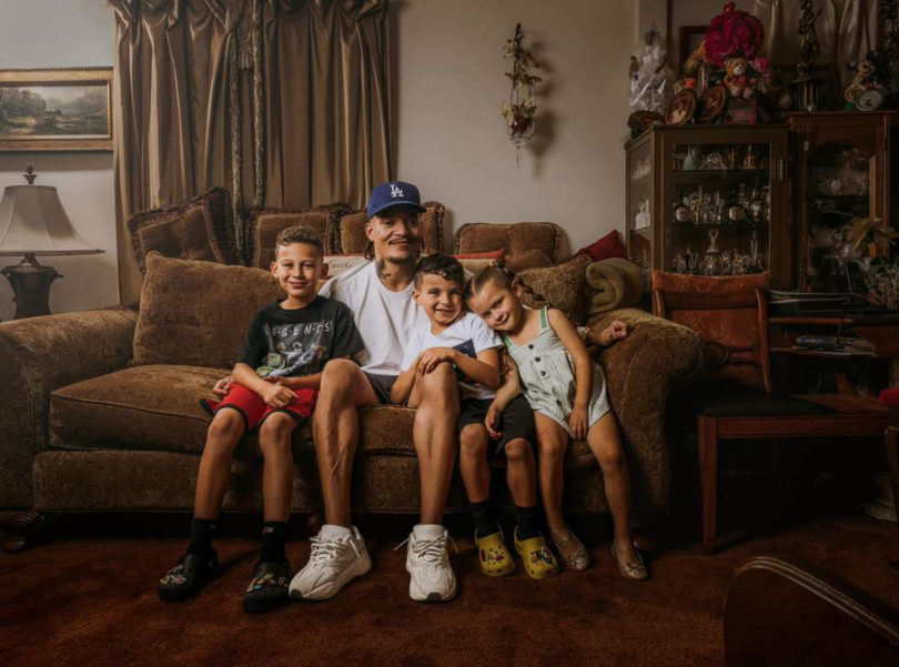 a man and his three children sit closely together on a sofa to have their photo taken