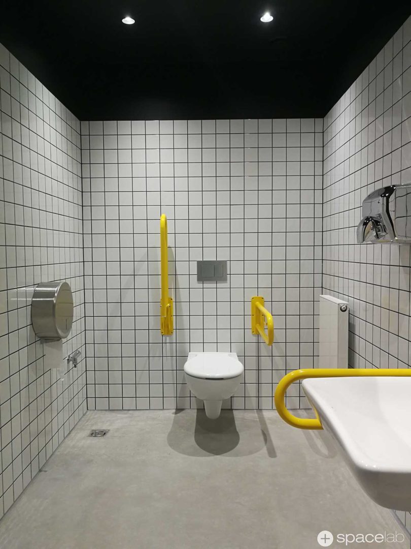 modern office bathroom with white tiles and yellow accents