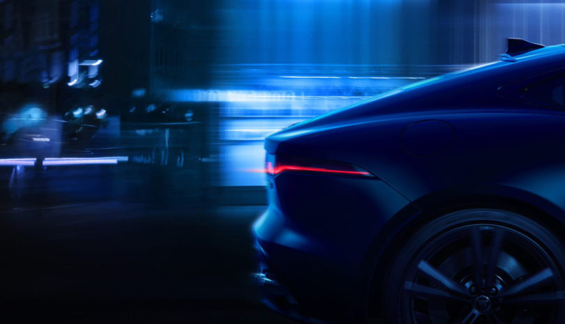 Rear of F-TYPE passing as a silhouette blur against nighttime city backdrop.
