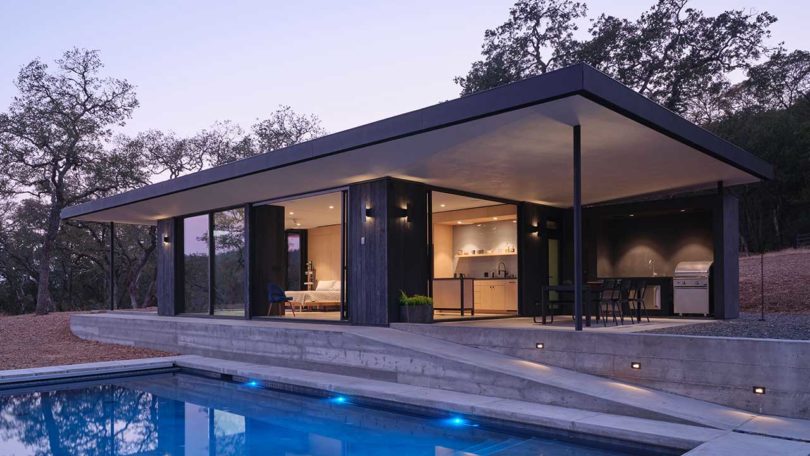 evening view of exterior view of small modern black house and pool
