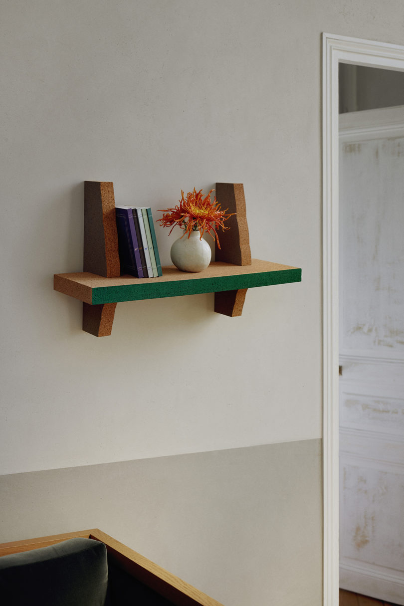 small wall shelf with green edging holding books and a vase with flowers