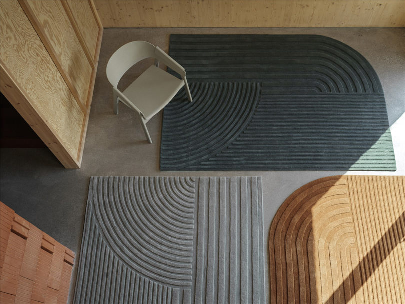 Overhead shot of dark sage green, burnt orange and light blue rugs with chair situated in upper lefthand corner.