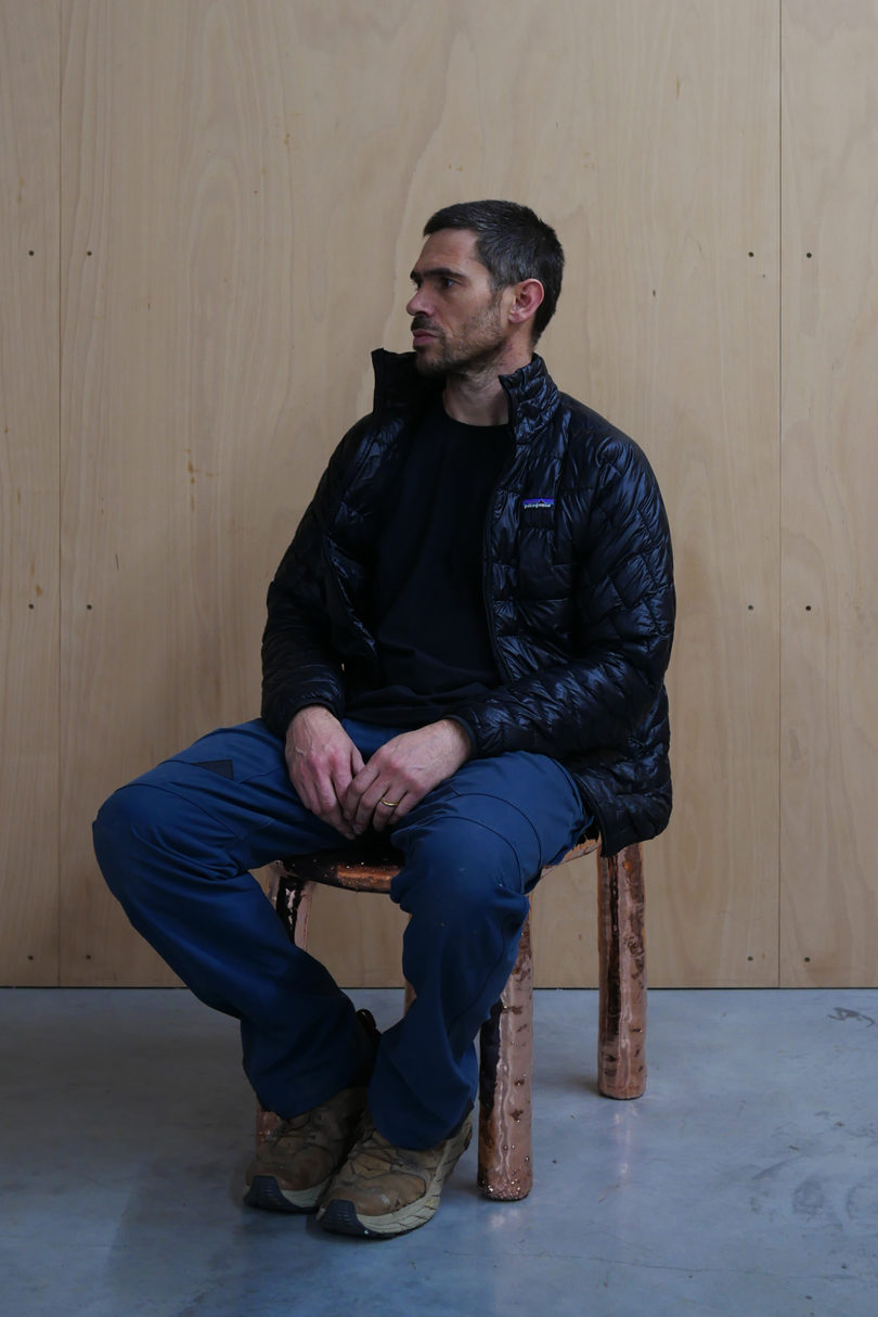 light-skinned man sitting in a chair casually wearing jeans and a dark jacket