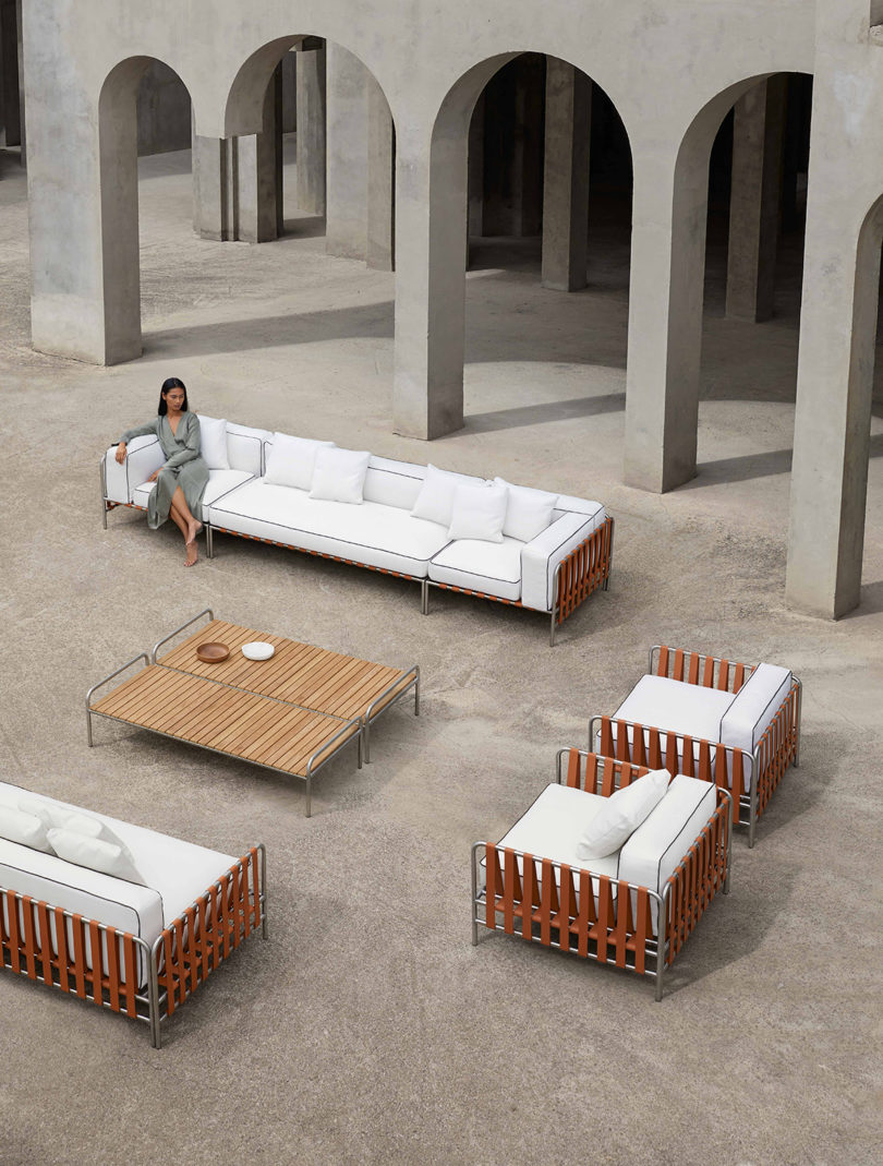 outdoor furniture collection with white upholstery arranged in an open space surrounded by a tan building with lots of arches