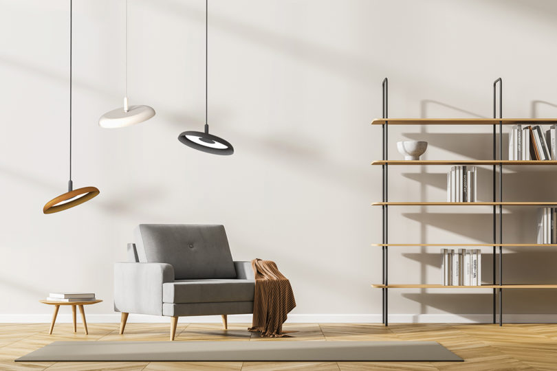 three disc-shaped pendant lights hanging over a grey lounge chair next to a wooden bookshelf