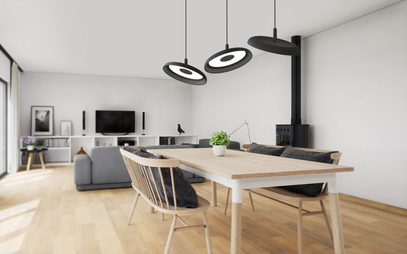 three black disc-shaped pendant lights hanging over a dining table and seating