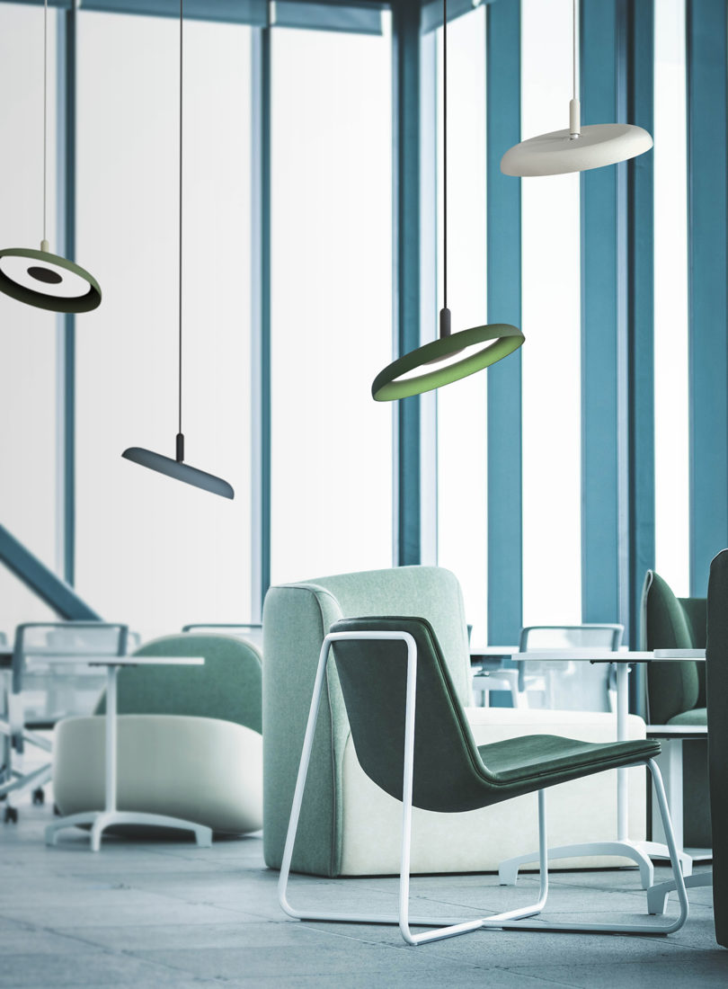 four different colored disc-shaped pendant lights hanging over seating in an office space with large floor to ceiling windows