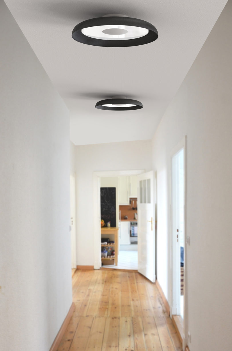 two black disc-shaped lights mounted to the ceiling in a long hallway