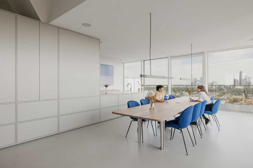 angled interior view of modern white kitchen with dining table with blue chairs