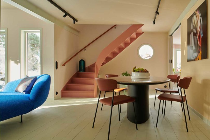small round dining table with four simple chairs in modern living space with stairs in background