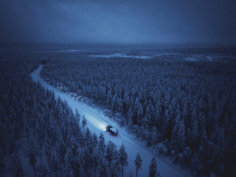 Lone electric truck delivering blocks of ice and snow driving across snowy Arctic Forest highway.