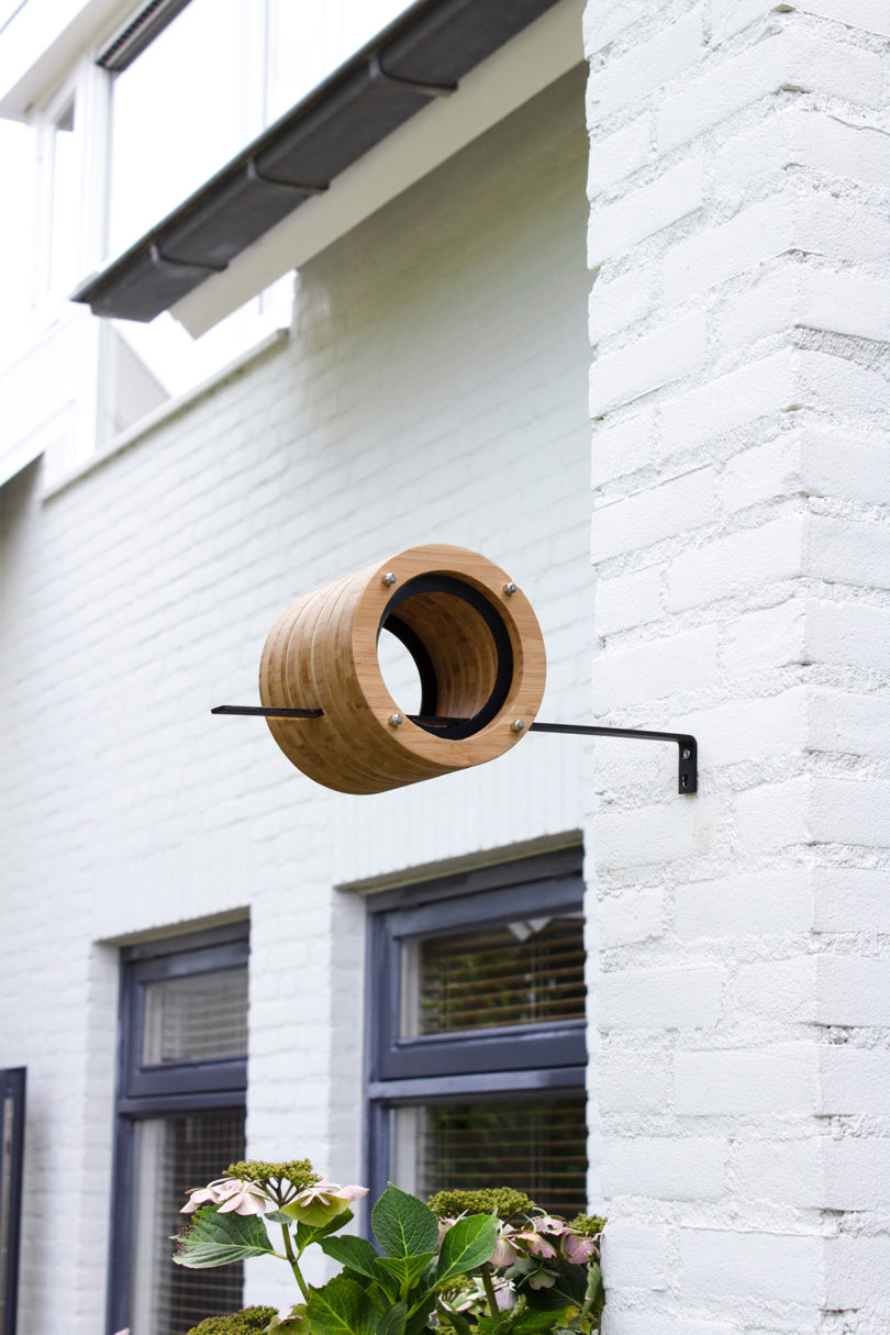 cylindrical bamboo bird feeder mounted on an exterior wall
