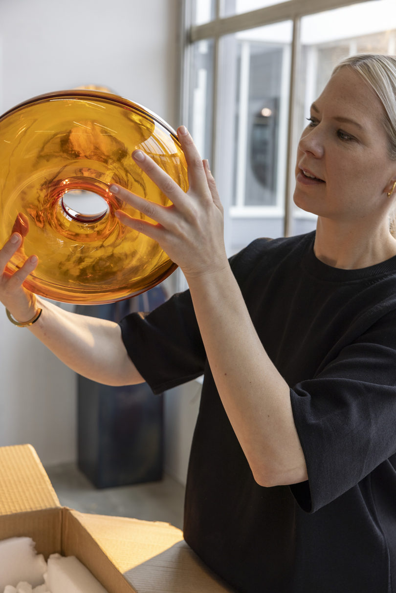 light-skinned woman wearing a black shirt holding up an orange donut-shaped object to examine