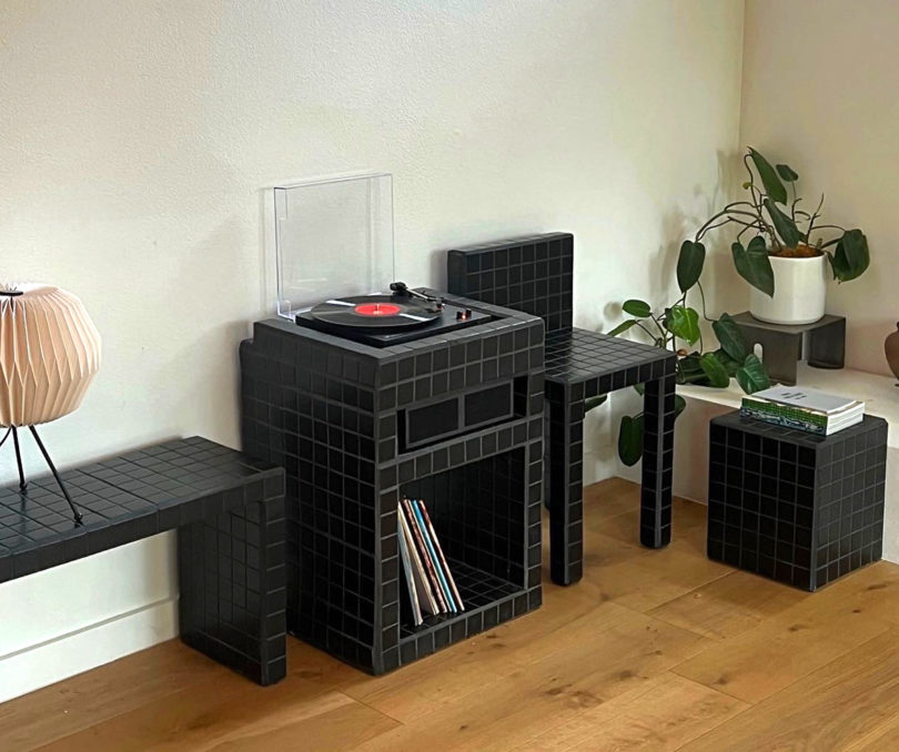 Amore Mio all-black turntable and speaker stand staged in a living room next to complementing black tile side table and chair.