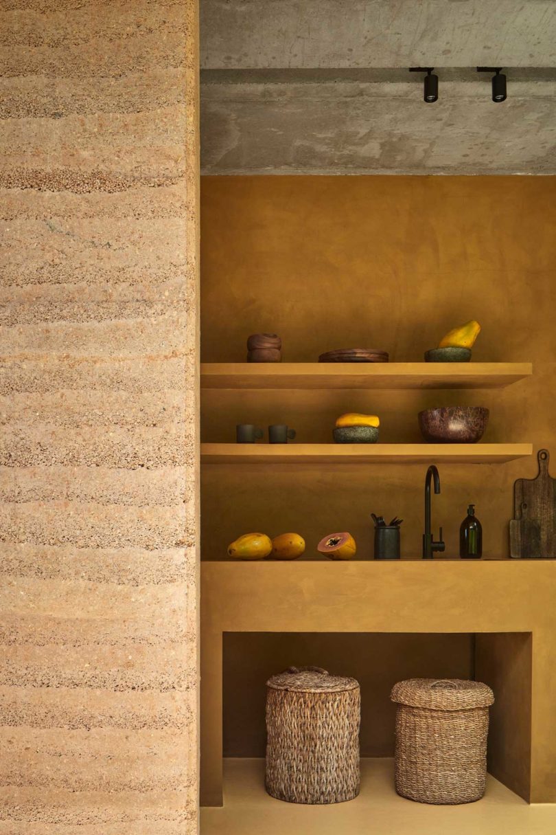 interior view of rammed earth wall with simple shelves holding dishes