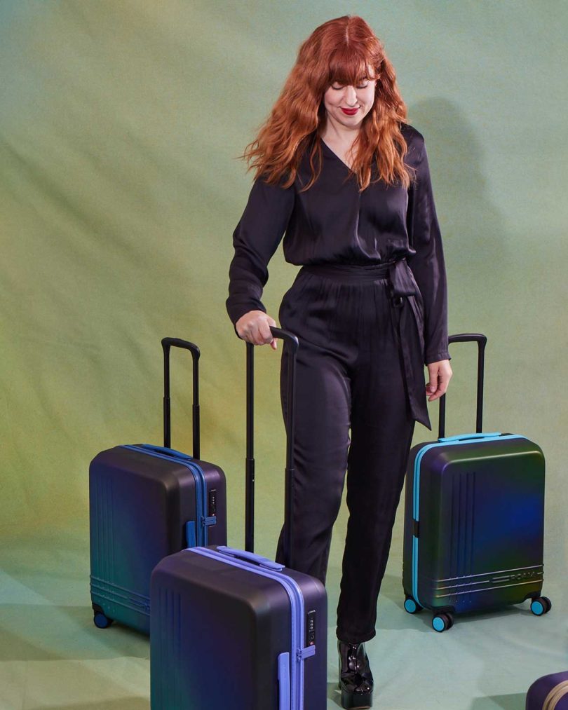 red-headed tattooist and artist Amanda Wachob standing with 3 hand-painted suitcases