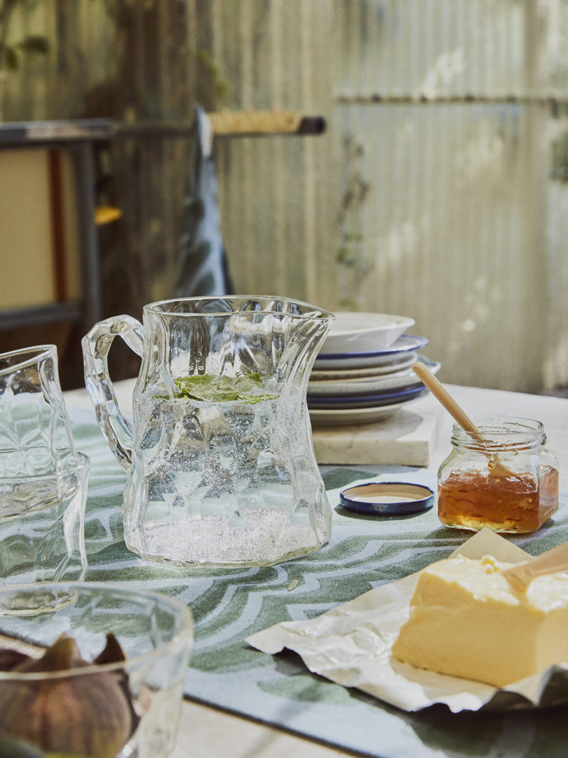 a styled table with dinnerware, honey, and a water pitcher and glasses