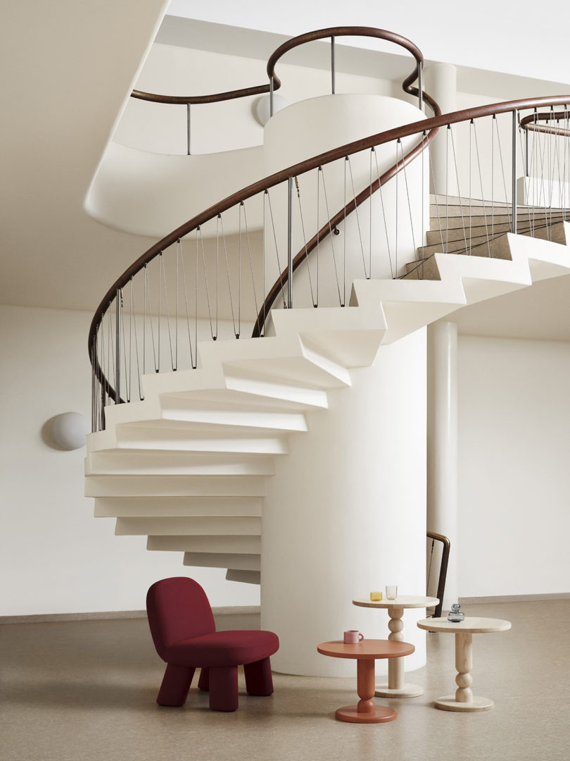 a modern chair and three side tables at the bottom of a sweeping white staircase