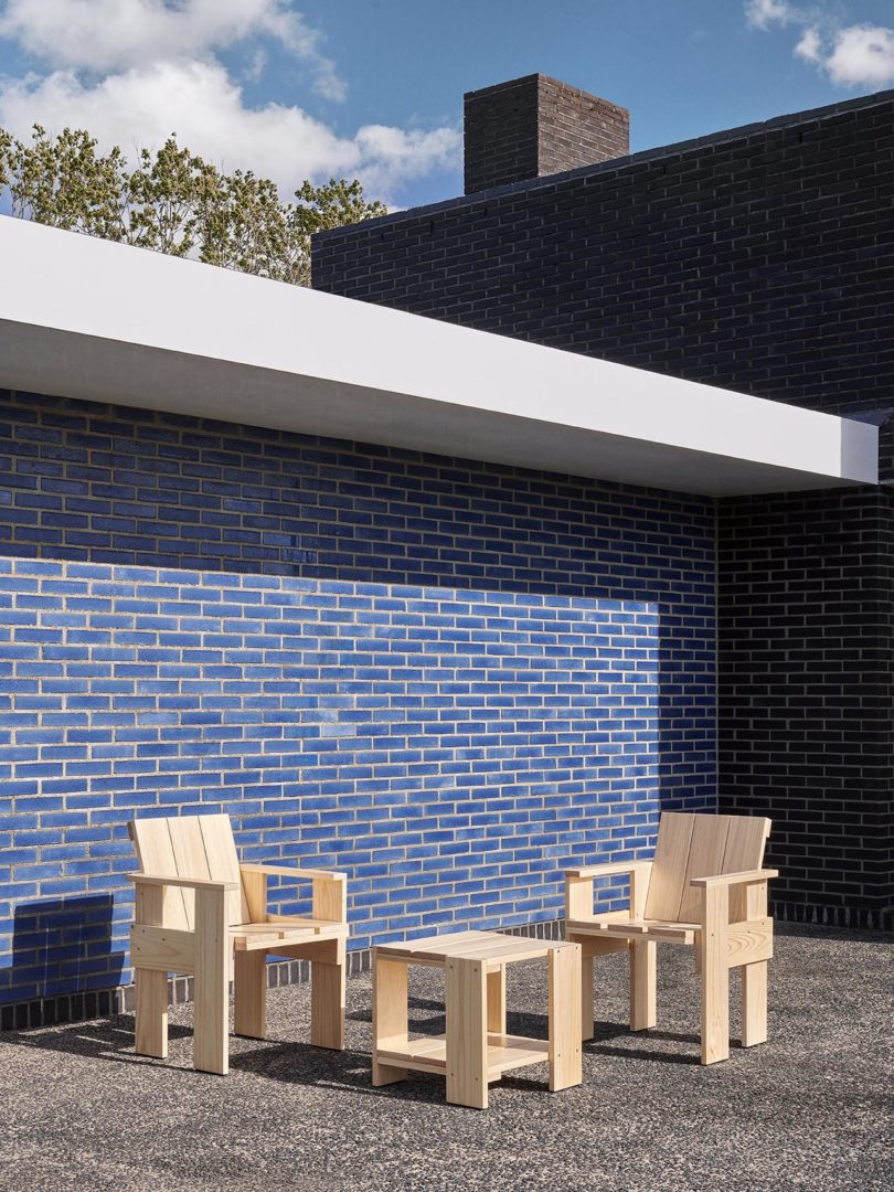 wood outdoor chairs and side table in front of blue tiled wall