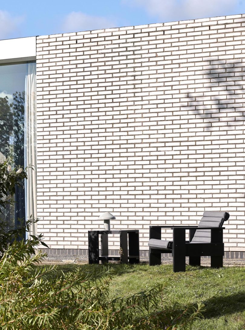 an armchair and side table sit outside in front of a white brick wall