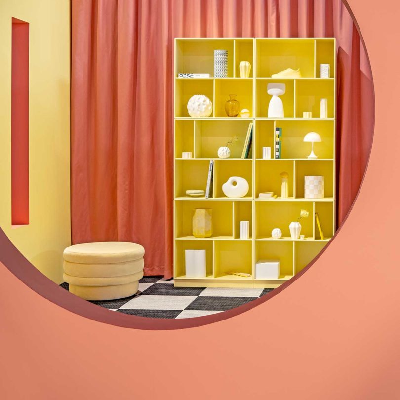 bold color-blocked exhibition looking through window cutout to yellow bookcase