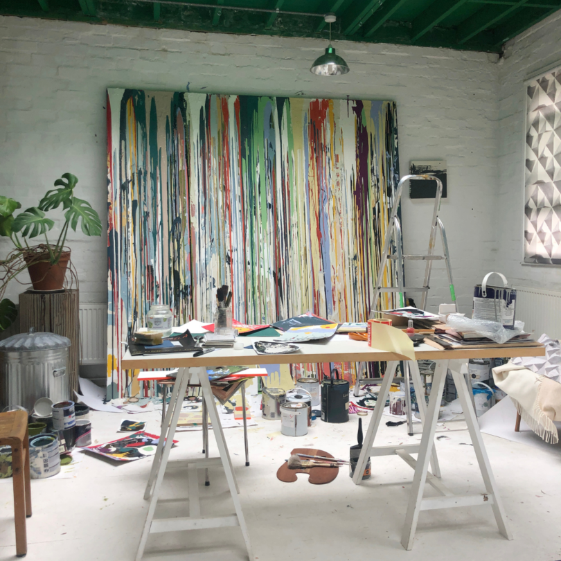 art studio with dripped paint canvas with desk and ladder and paint scattered