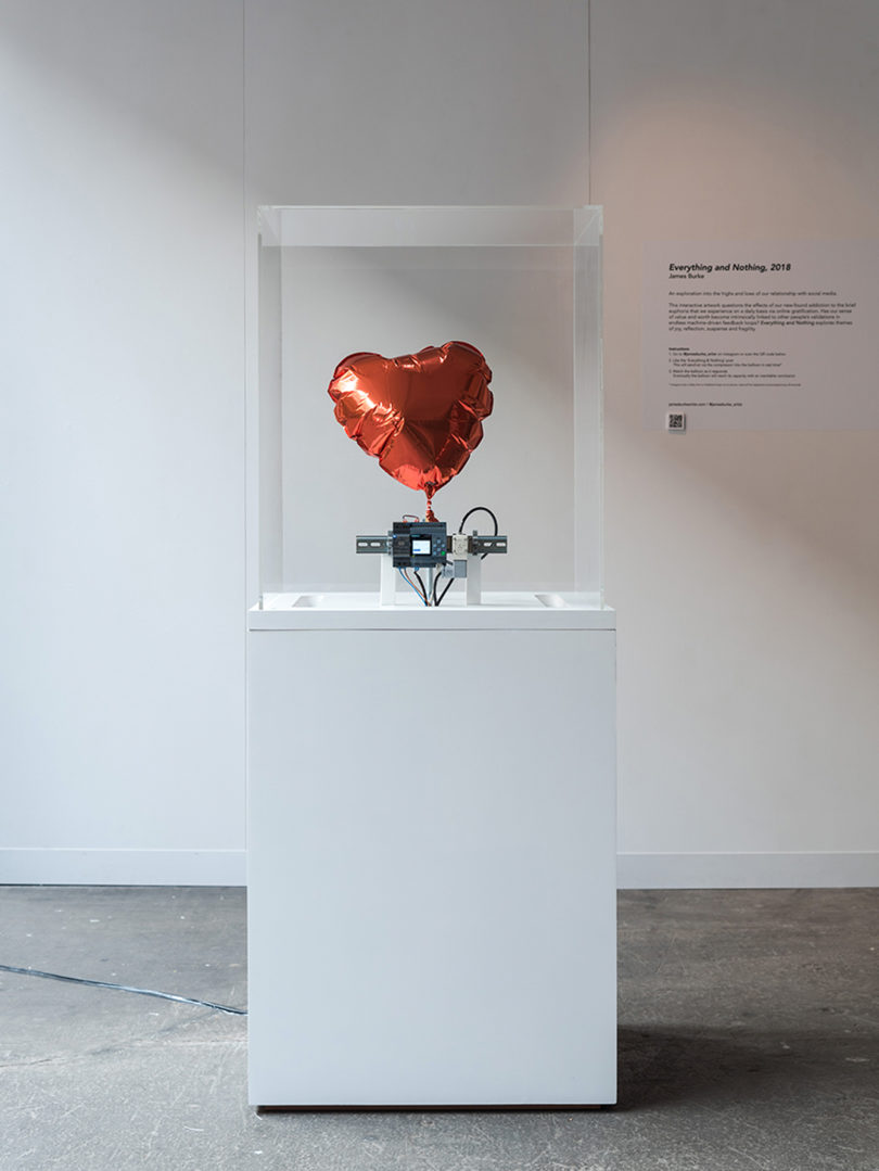 a red mylar heart balloon encased in glass on a white pedestal