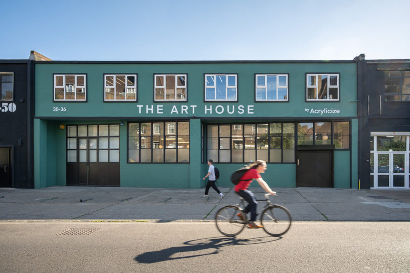 a person rides a bike in front of a teal colored building that reads THE ART HOUSE