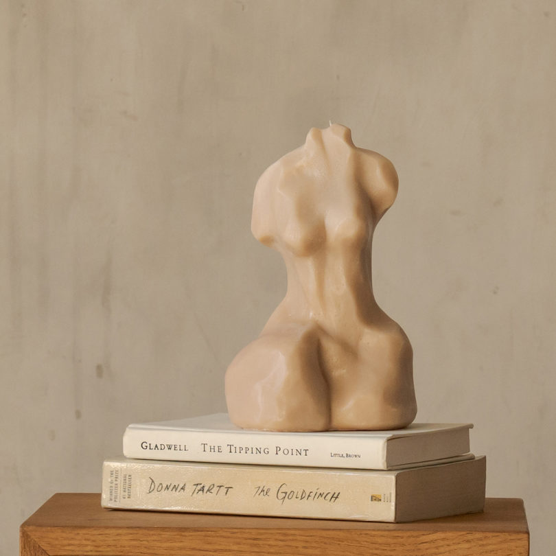 beige candle in the form of a female silhouette sitting on top of two books