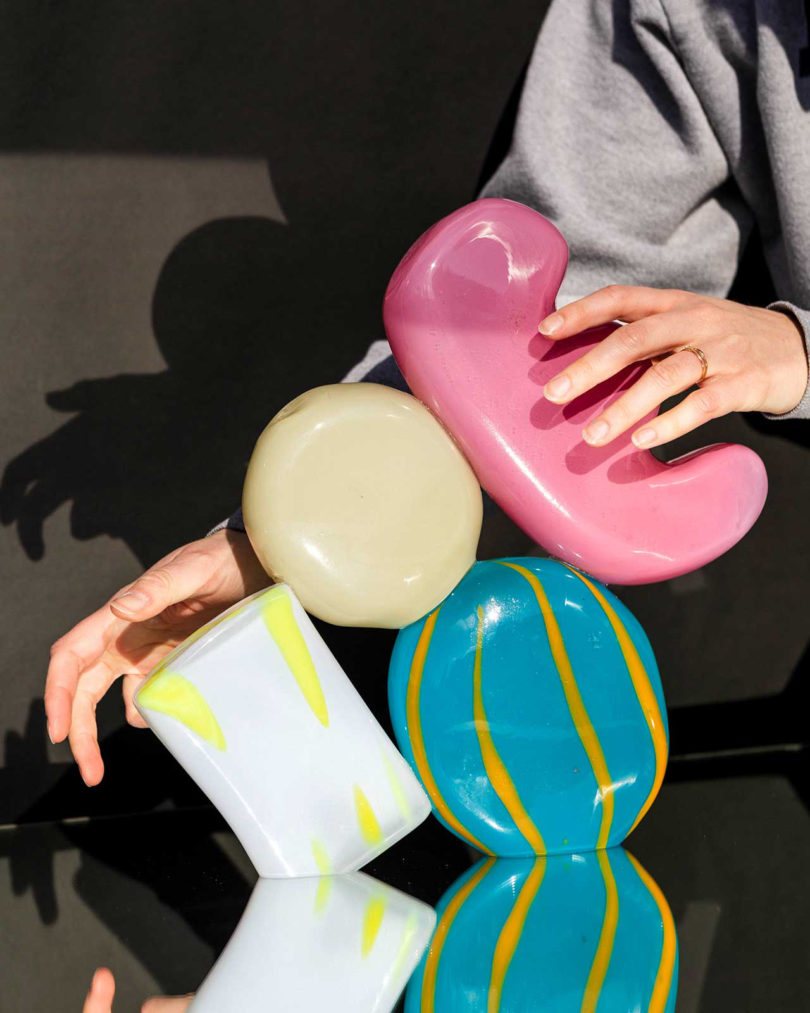 two hands holding a blue, cream, white, and pink stacked glass sculpture