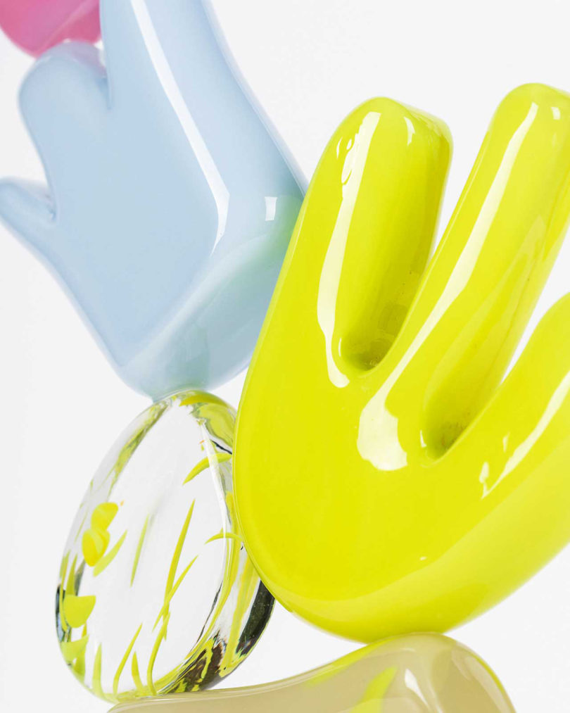 detail of two hands holding a blue, lavender, yellow, beige, and pink stacked glass sculpture