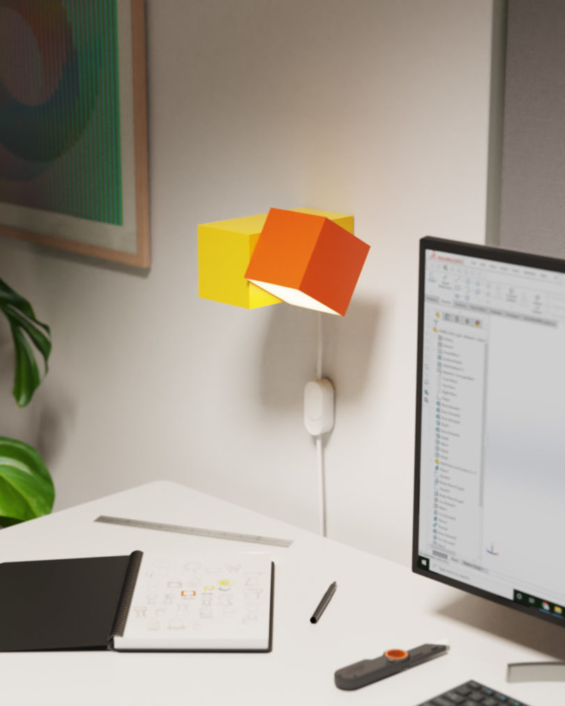 Wall mounted Analog desk lamp in orange and yellow on white desk situated to the left of a computer screen.