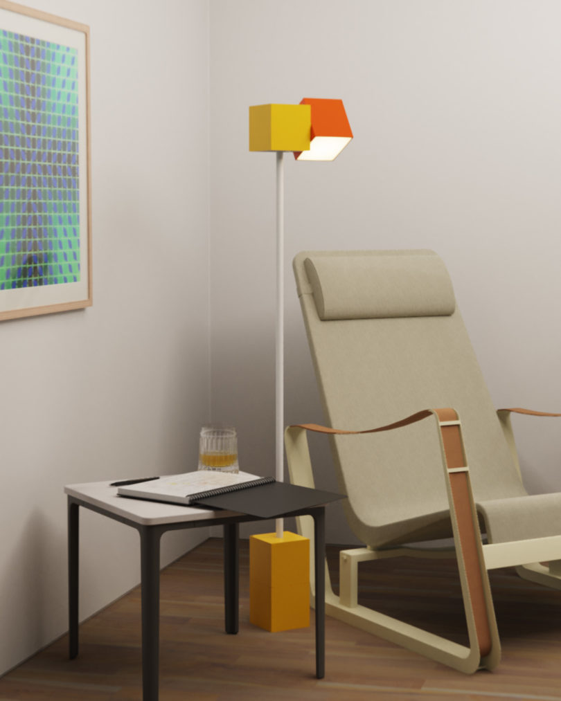 Analog floor lamp in orange and yellow near modern arm chair and side table in the corner of a room with white walls.