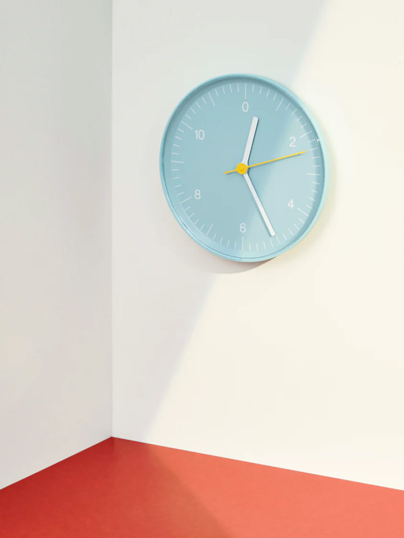 Light blue HAY wall clock hung on wall near corner with orange-red flooring.