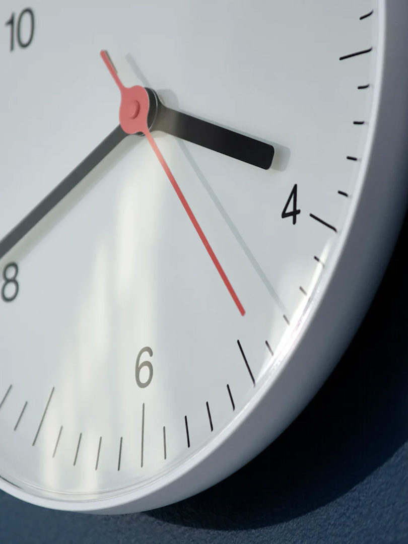 Close up detail of gray analog wall clock with white face and black hour and minute arms, with red seconds arms, against black background.
