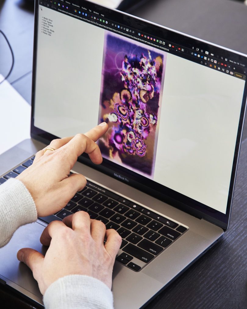 a light-skinned hand points to a predominantly purple design on a laptop screen