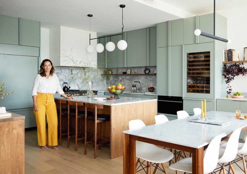 woman standing in apartment with angled view of modern dining room and kitchen in pale green