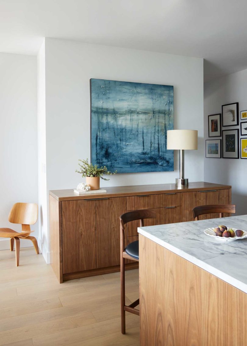 نمای زاویه‌دار فضای داخلی مدرن که از پشت میله آشپزخانه تا کریدنزای چوبی با نقاشی آبی روی آن است