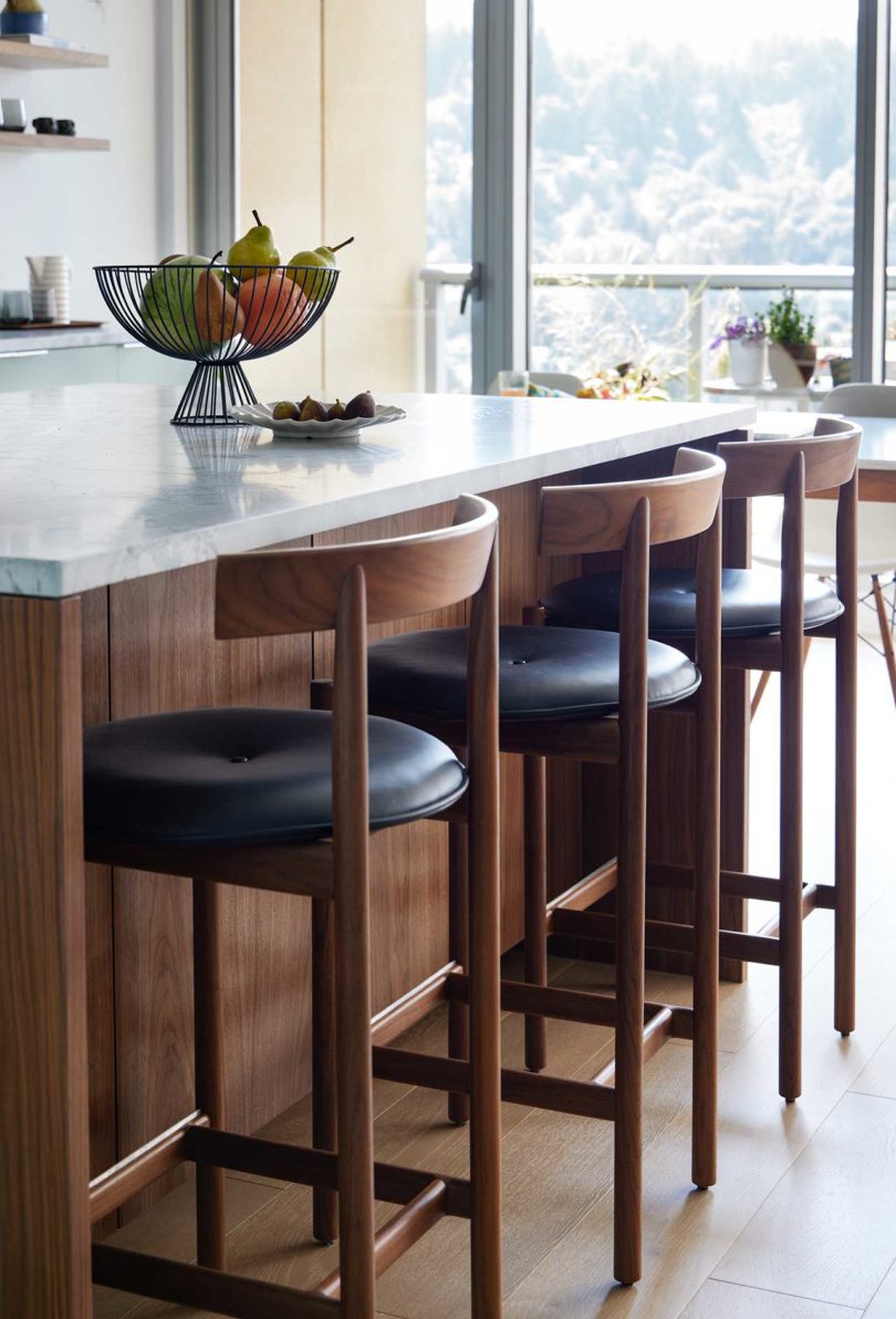 angled side view of multiple wood and black leather bar stools pulled up to kitchen island bar