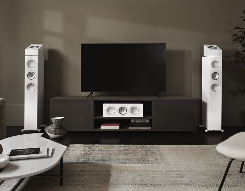 Two floor and one center KEF R5 HiFi speakers in white gloss finish set surrounding a home theater console with 55" television in between speakers.