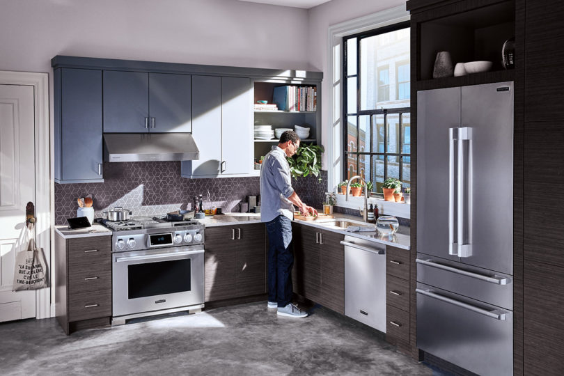 small modern kitchen with stainless appliances and a man preparing food at the counter