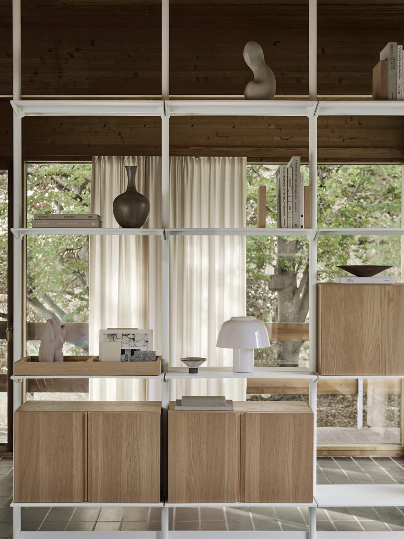 White String Furniture shelving with light wood veneer cabinet door set in living space with windows in the background and tile flooring.