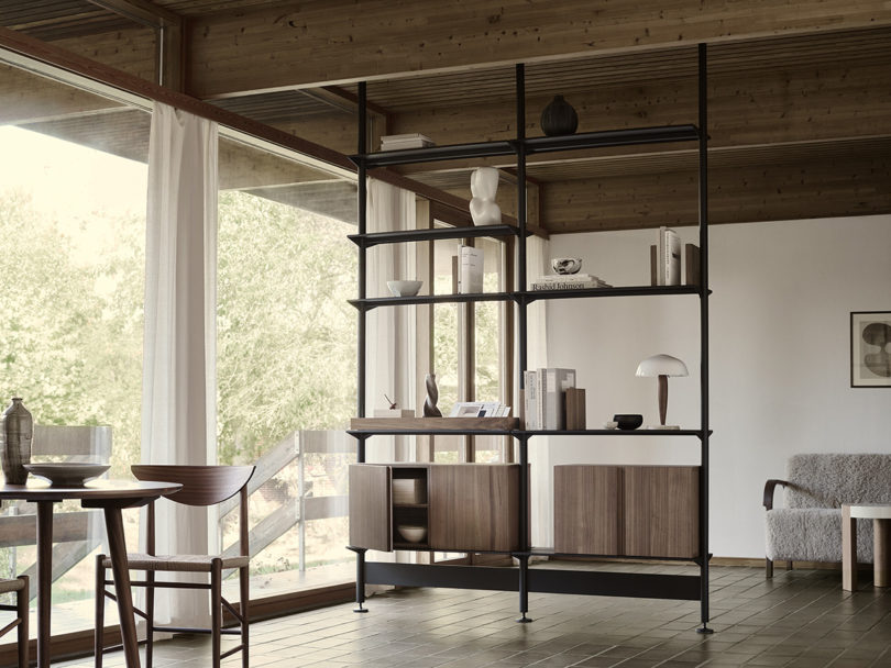 Black String Furniture shelving with light wood veneer cabinet door set in living space with windows in the background and tile flooring.