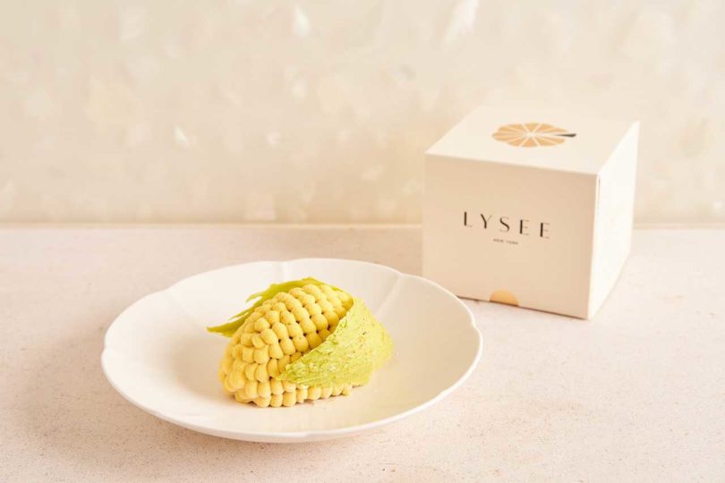 a corn looking pastry on a white plate with box in the background