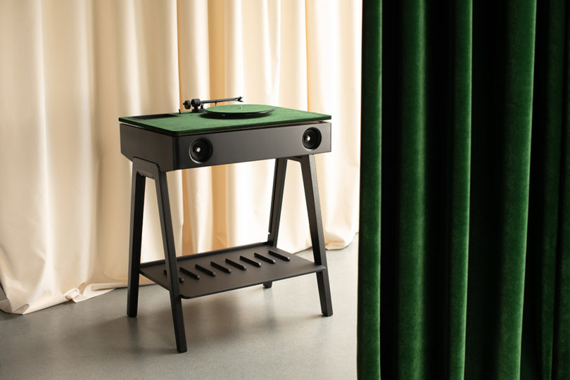 Green Riga corduroy velvet topped turntable and speaker system set in room surrounded by curtain backdrops.