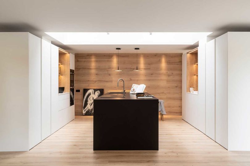 interior shot of modern home's kitchen with white cabinets, black island, and wood back wall