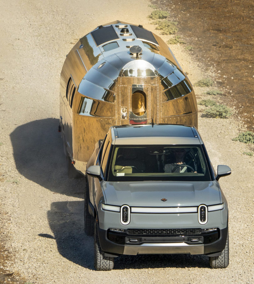 Bowlus Volterra RV being towed down a dirt road behind a Rivian EV in slate blue.