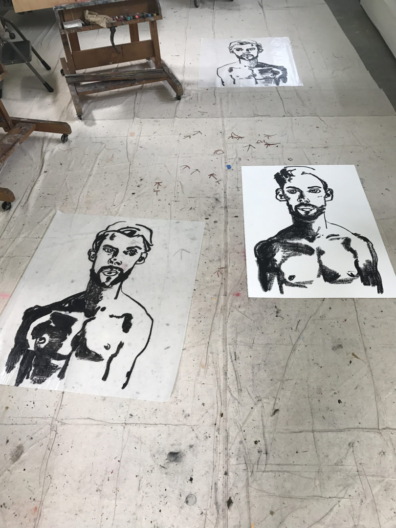 black portrait sketches on white paper laying on a studio floor