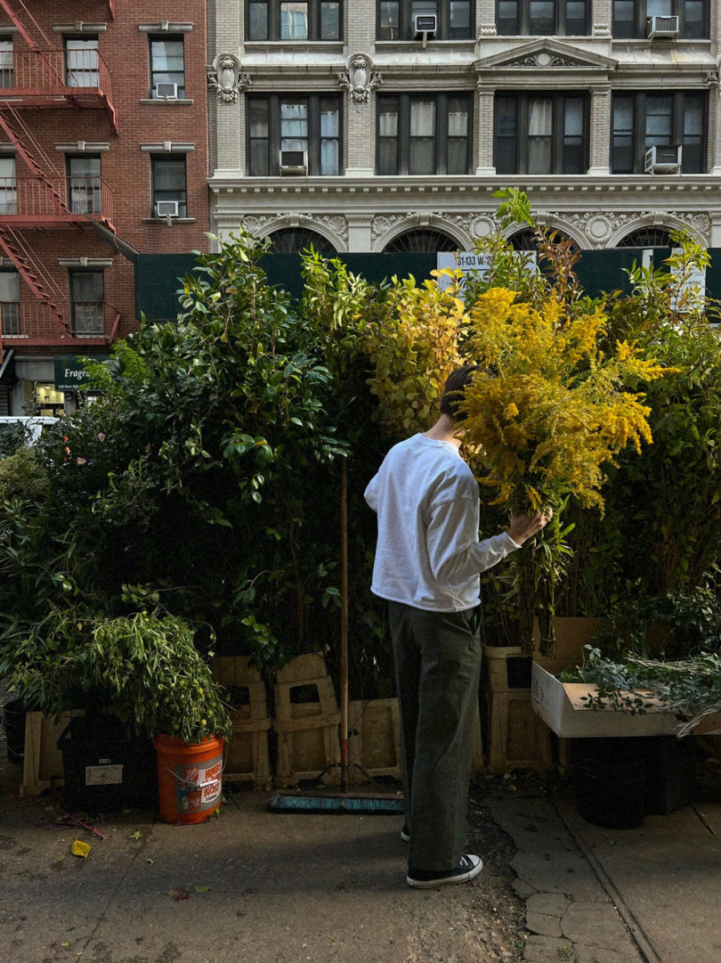 a man faces away from the camera picking out large greenery at a flower market