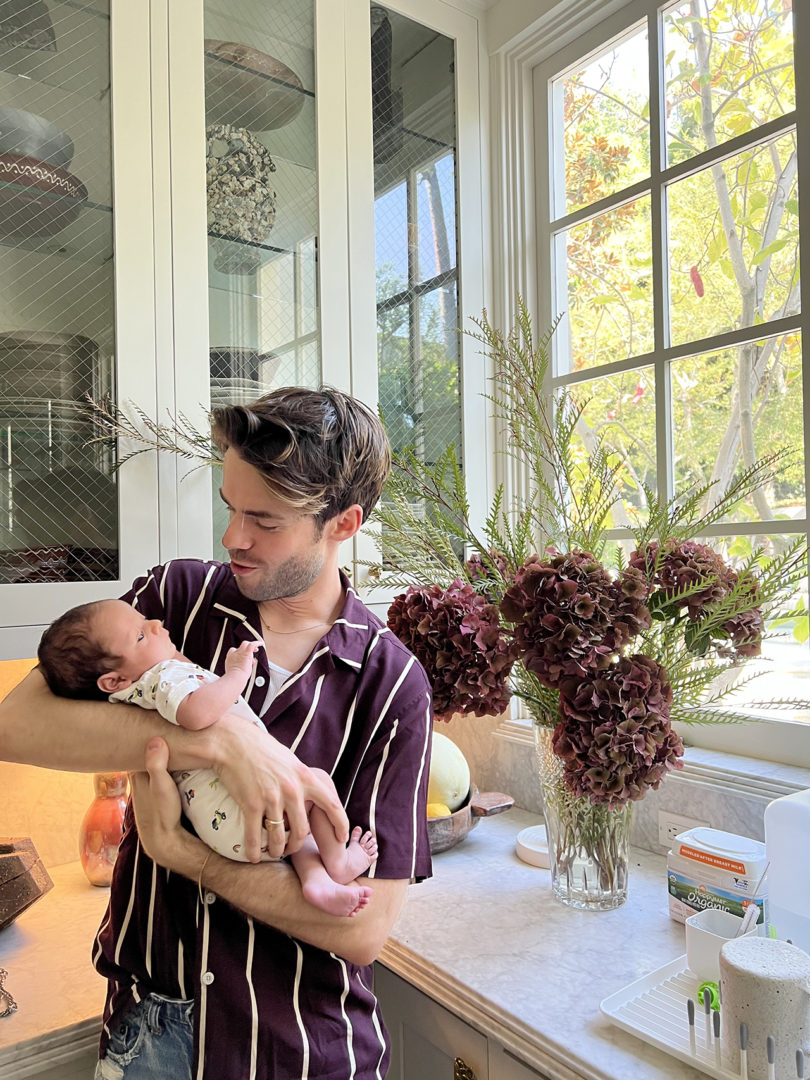 light-skinned man with dark hair and striped short-sleeved button down holds a light-skinned baby